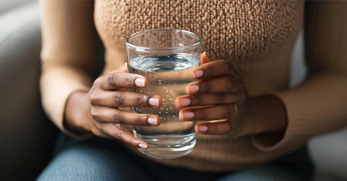 woman holding glass of water in front of stomach, concept of Crohn's & Ulcerative Colitis: