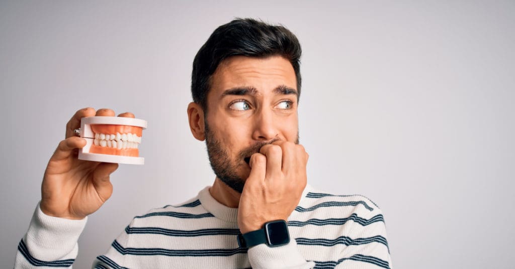 Man stressed holding a dental anatomy piece for the concept of Managing Dental Anxiety: Tips for a Stress-Free Dental Visit