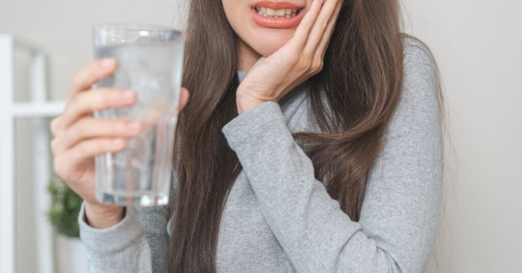 girl holding glass of water with ice and experiencing Sudden Tooth Sensitivity to Cold
